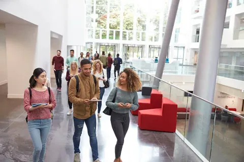 Students walking and talking in the glass-roofed atrium of a modern further education campus building